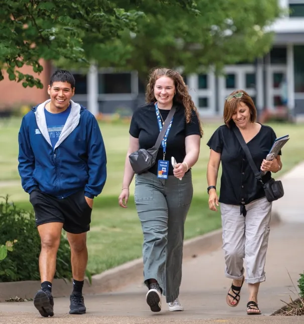 Three individuals walking across campus on a tour.